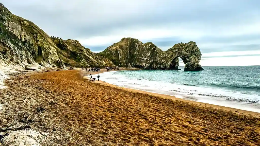 Limestone formation Durdle Door. Sandy bay, grey-green cliffs and a rock gate in the sea