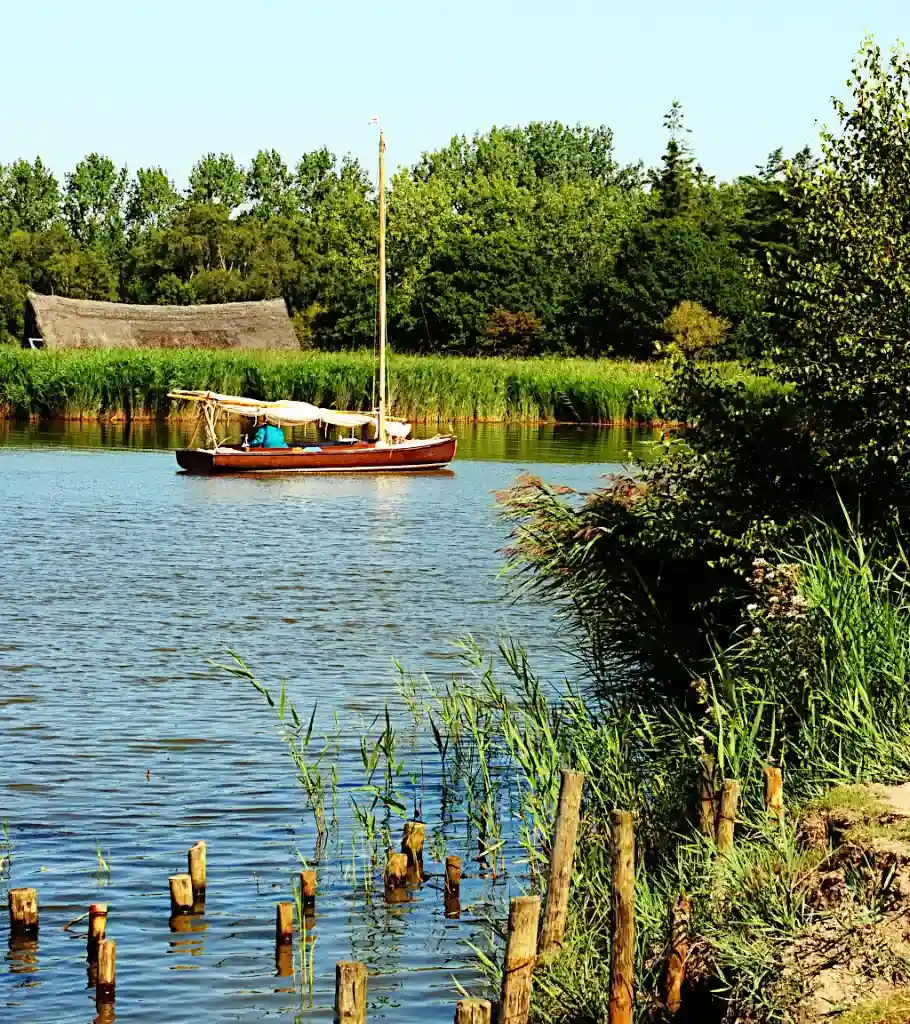 Sailboat on an inland waterway, lined with trees and shore vegetation