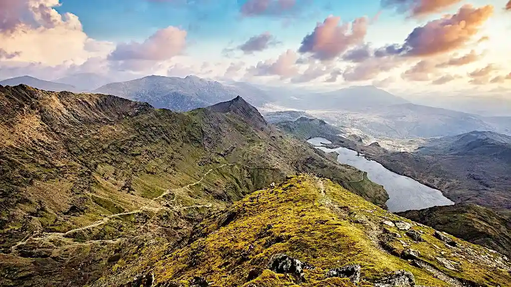 Sunset over mountain lake and green overgrown hill range in the mountains of Snowdownia National Park