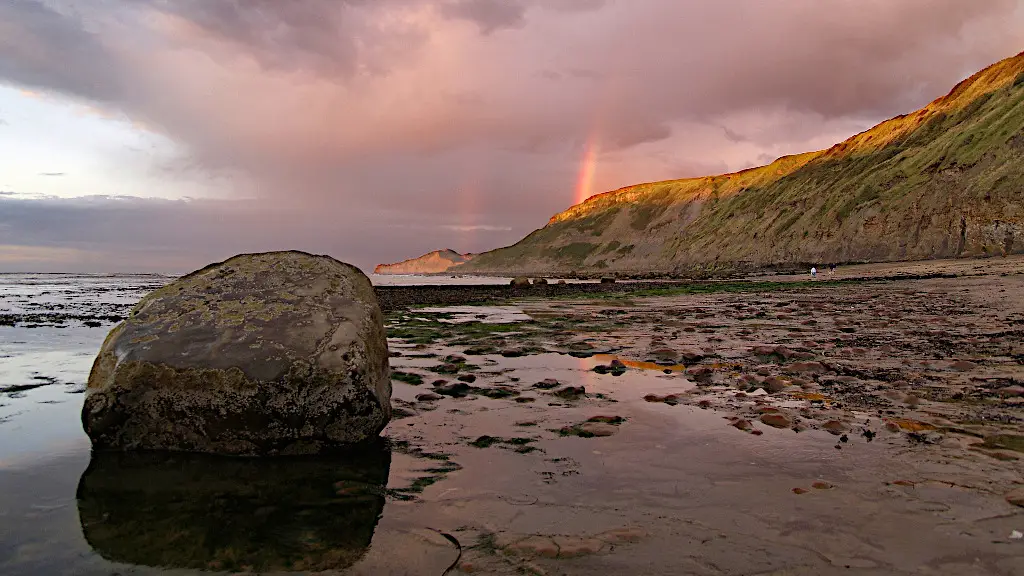 Great rock on the beach with cliffs in the background at sunset