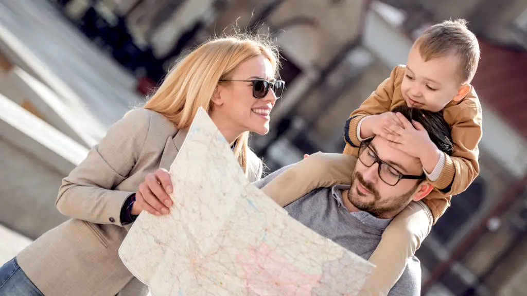 Mother, father and kid on shoulder of father looking happily at a map