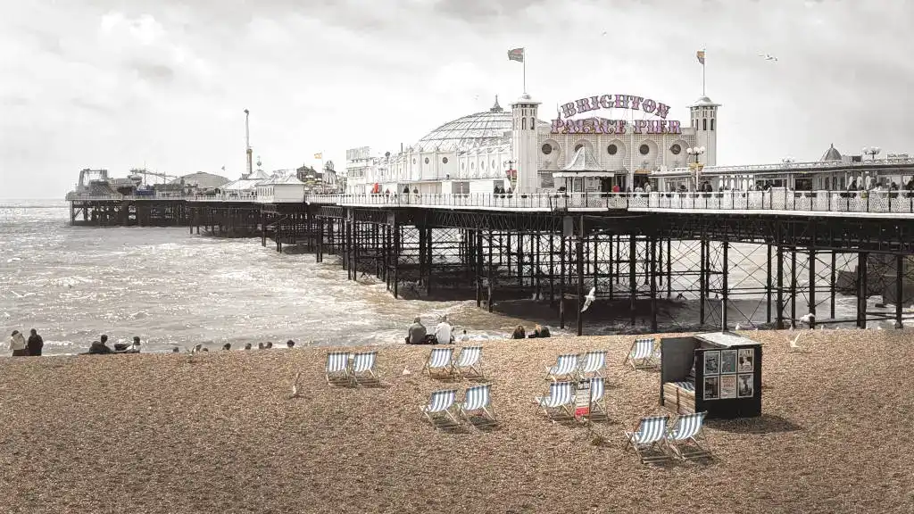 Brighton Palace Pier and shingle beach with beach chairs and tourists looking out at sea